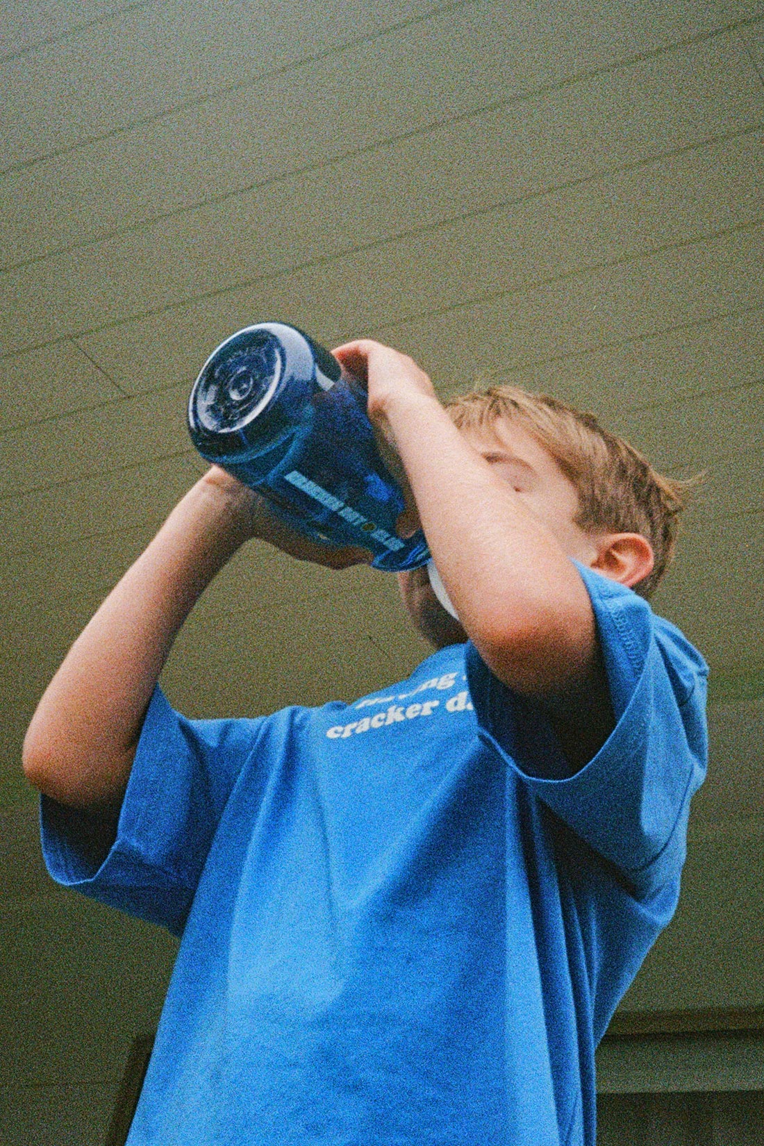 a little boy drinking from a blue cracker day 1 litre drink bottle wearing a blue tee shirt