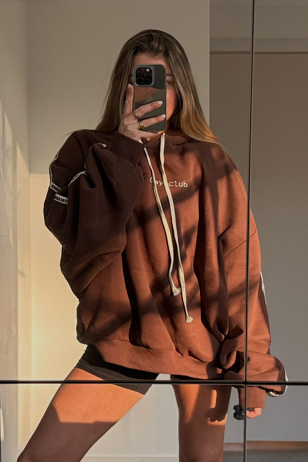 cloud racer hoodie in brown by cracker day club worn with workout shorts in front of a mirror