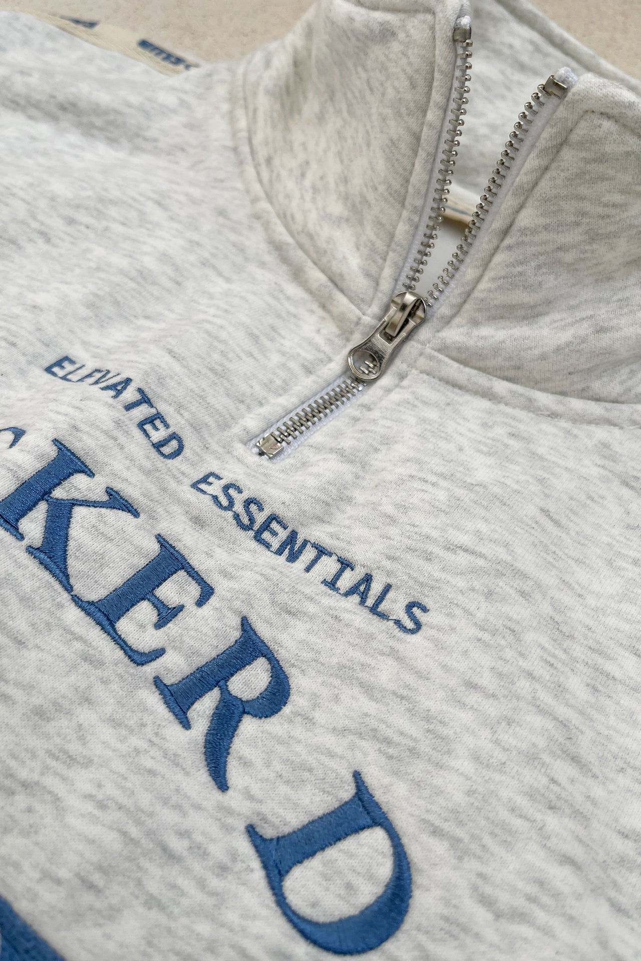 Person wearing a white sweatshirt with text and pants, holding a black bag against a light wooden wall.