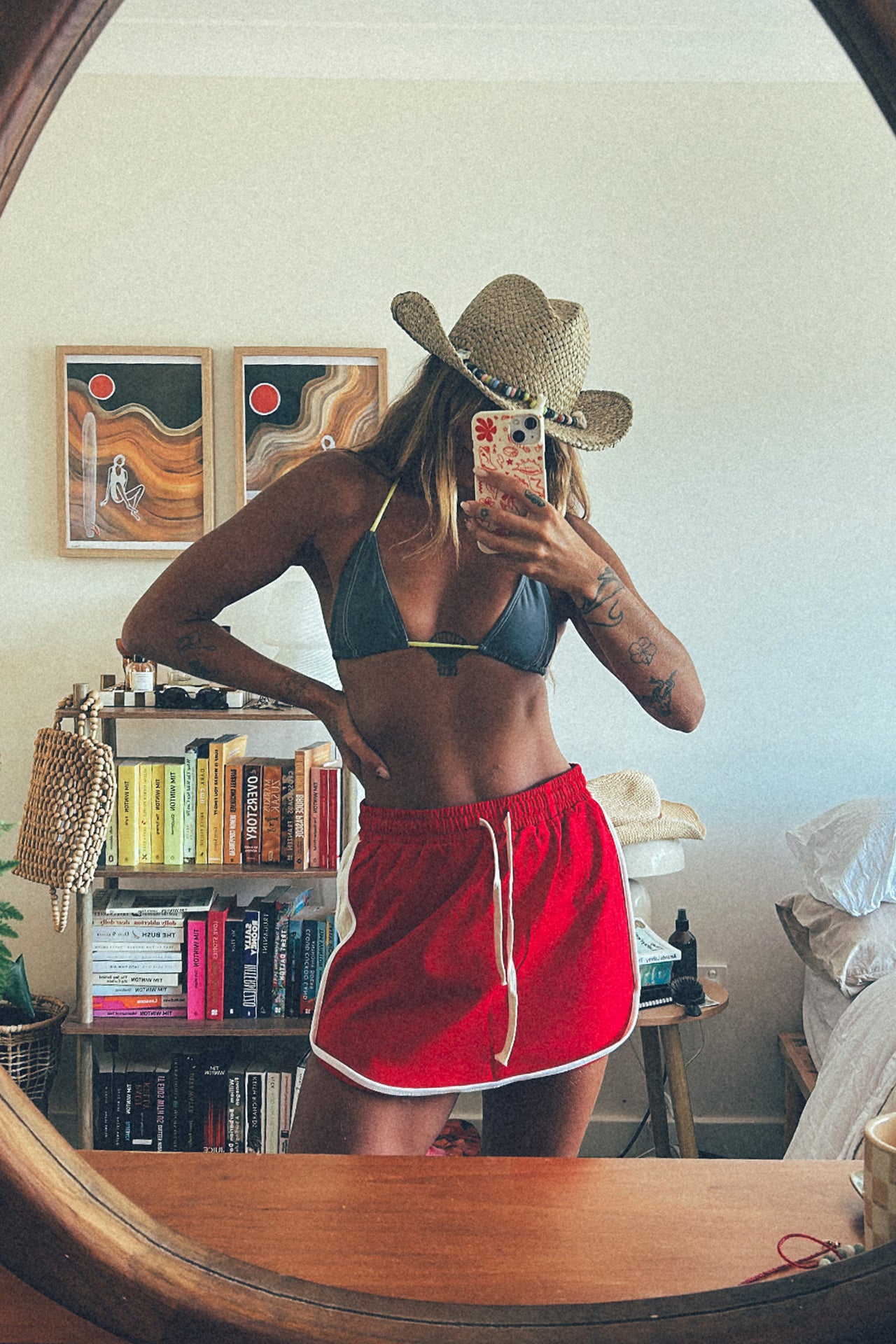 Woman wearing a straw hat with beads and a red swimsuit, sitting on a yellow chair.