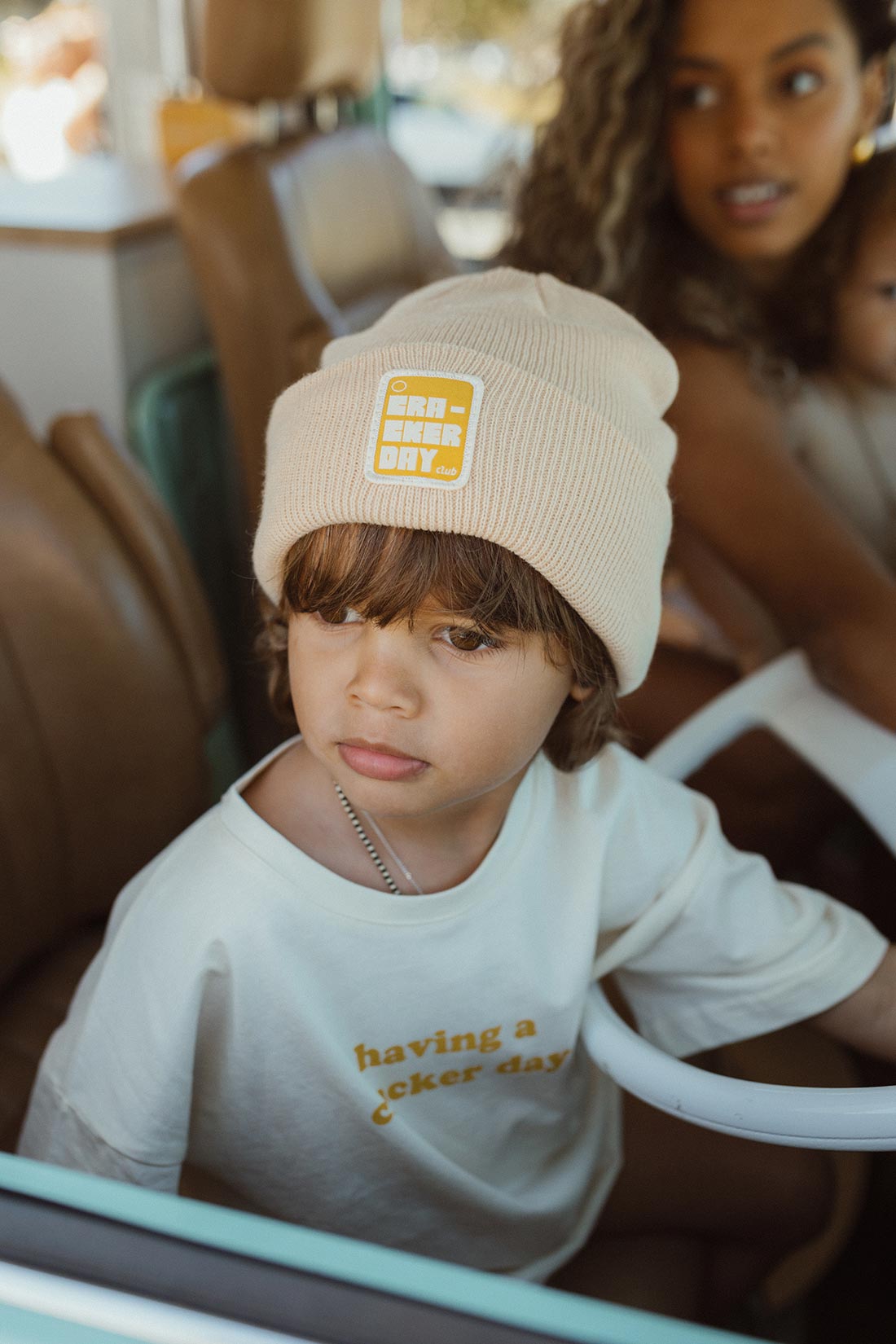 Boy wearing a cracker day club stacked beanie in a retro campervan with his mum and baby sister