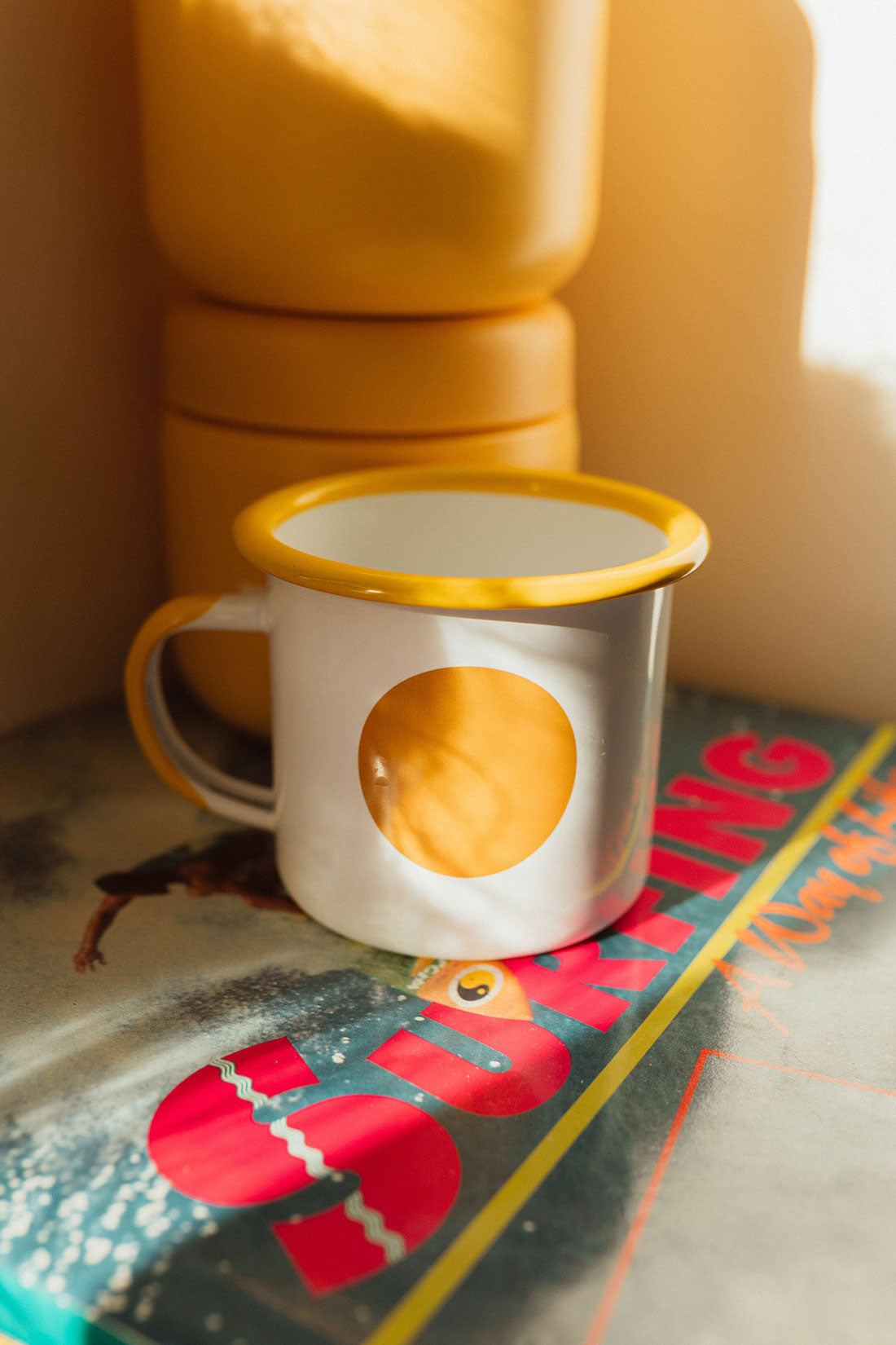 The suns up travellers cup sitting on an old surfing magazine in a campervan caravan. It has yellow rim and circle sun mofif.