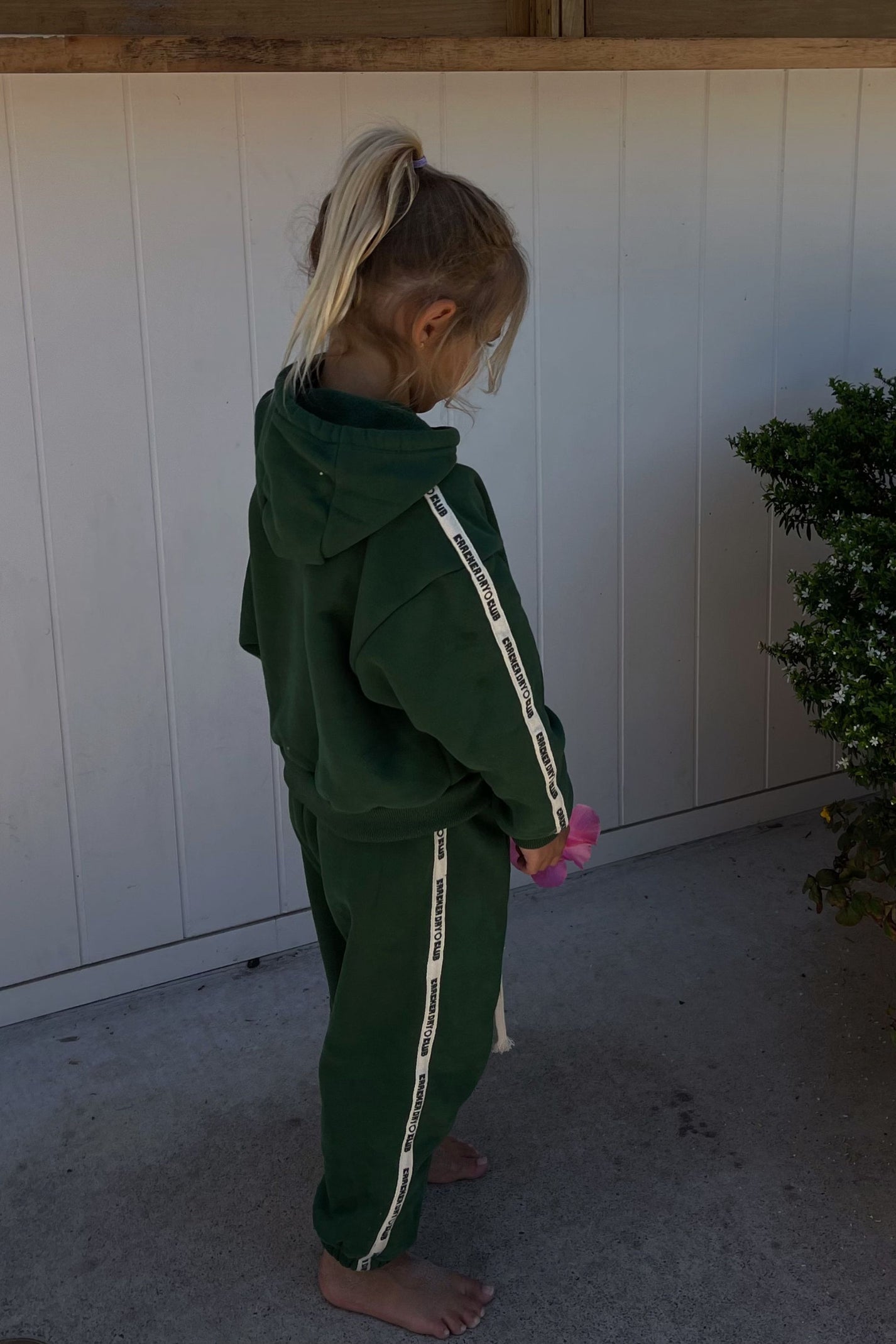 young girl wearing forest green sweatpants and sweater holding a flower by cracker day club