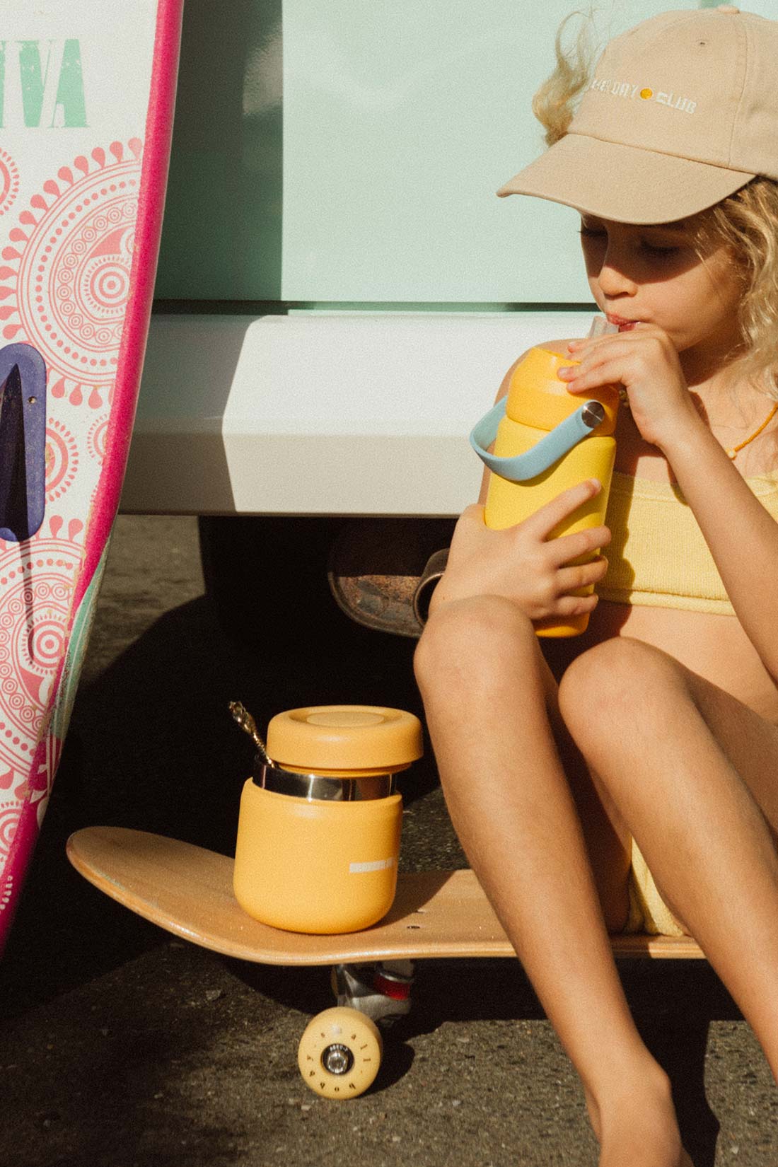young girl sitting on a skateboard drinking from a cracker day club yellow insulated drink bottle with silicone mouth piece