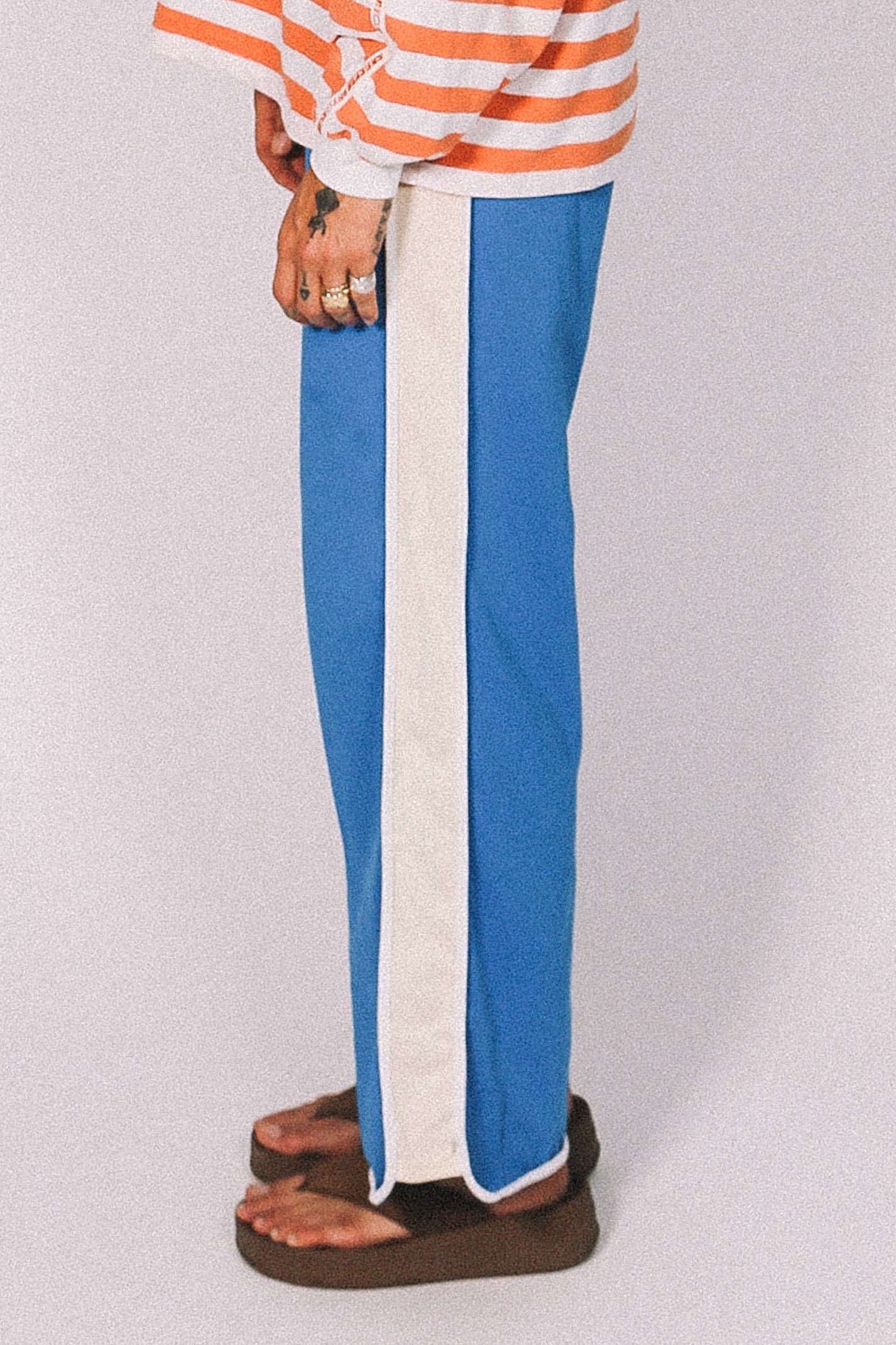Person wearing blue pants with a white stripe and an orange and white striped shirt on a light gray background.