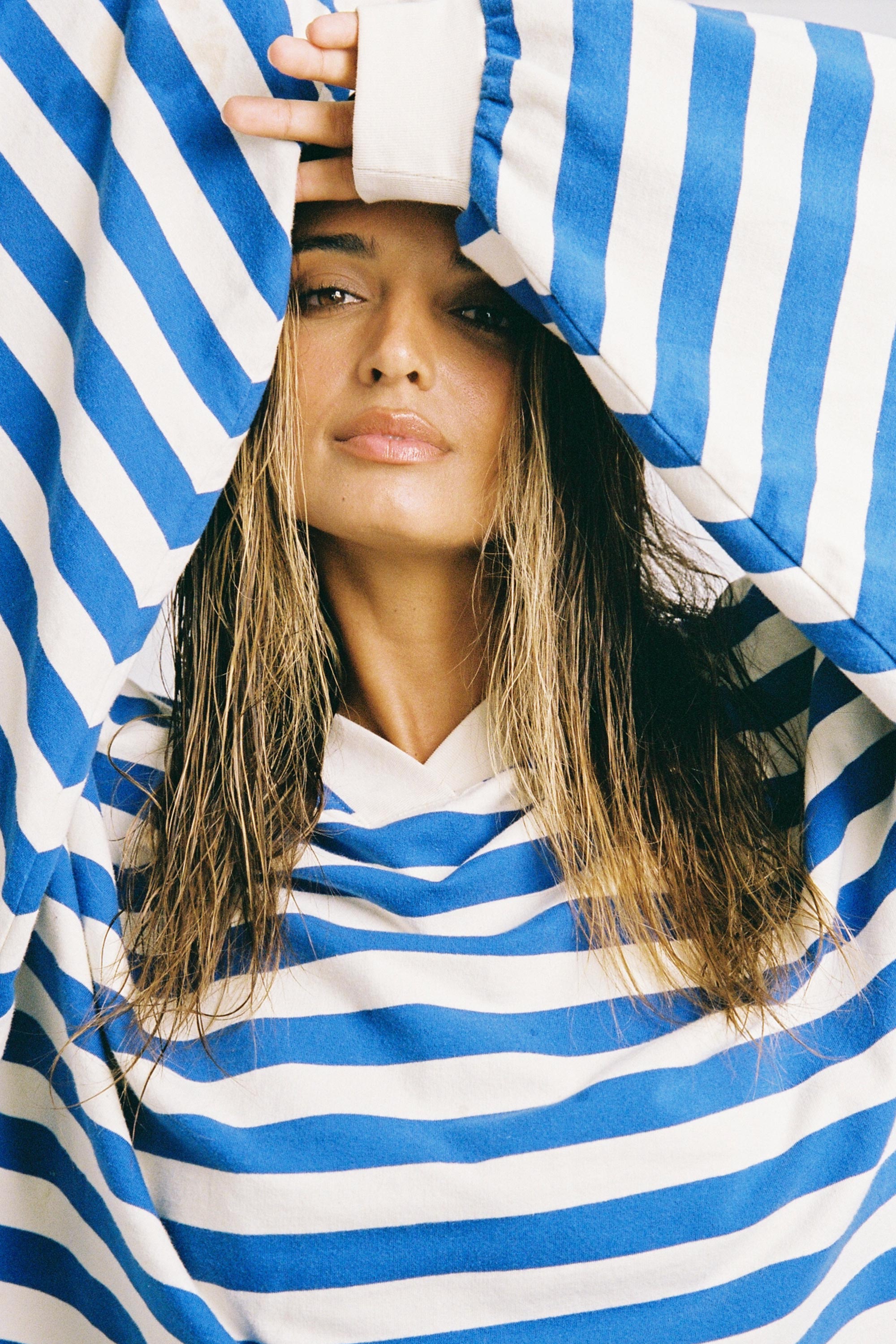 Woman wearing a blue and white striped shirt with a hood, holding the hood over her head.
