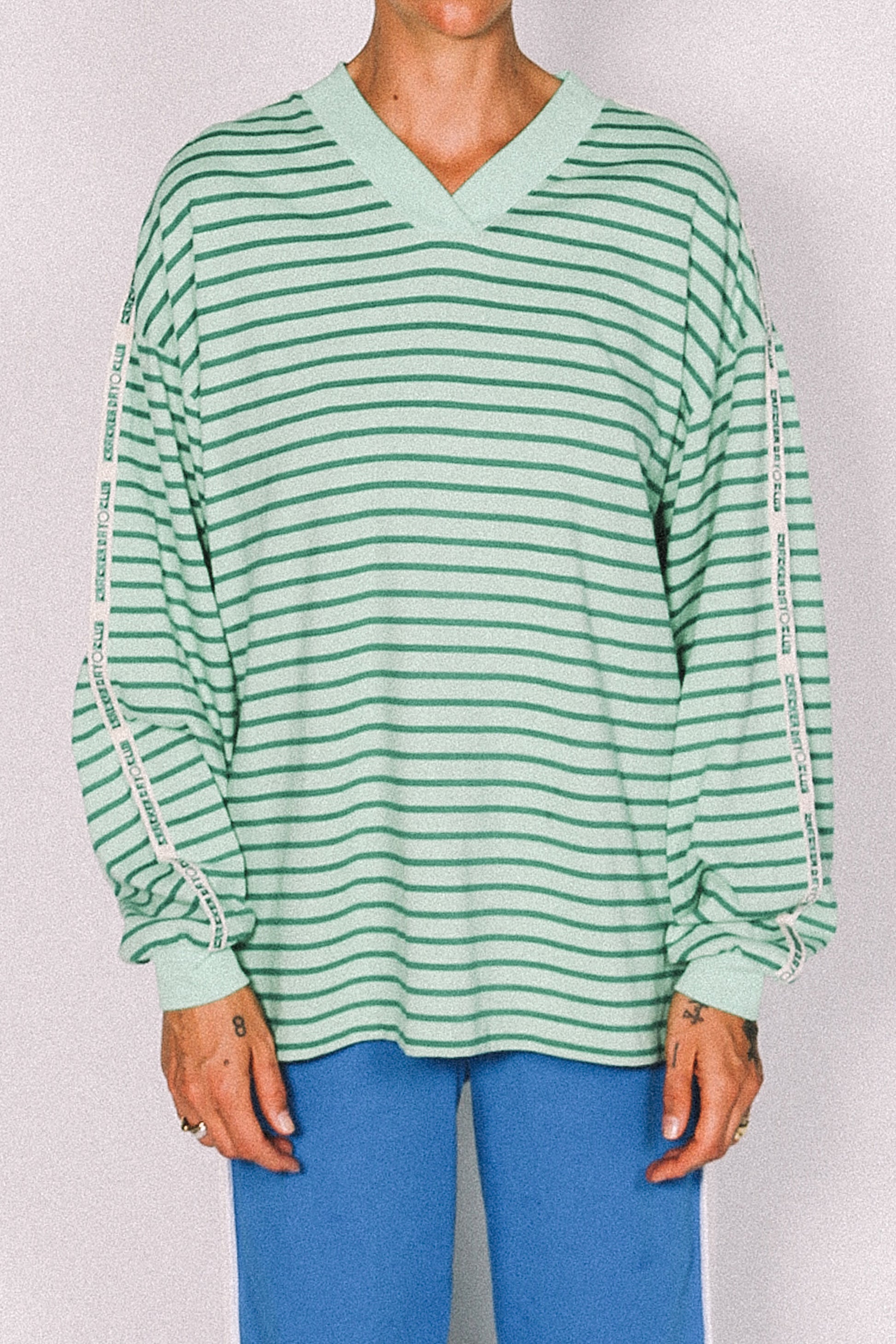 Green and white striped long-sleeve top worn by a person on a plain background