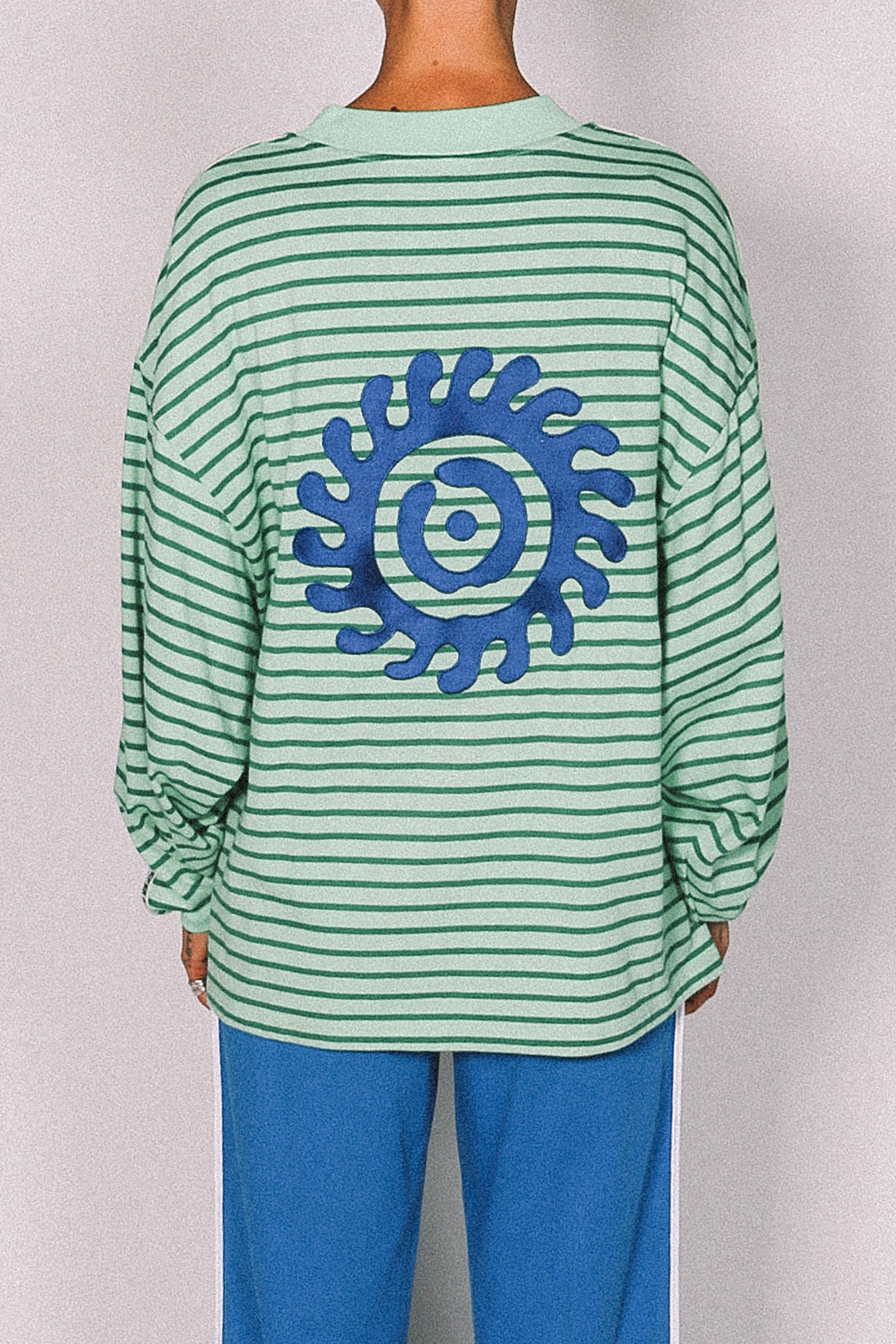 Green and white striped long-sleeve shirt with a blue circular design on a plain background