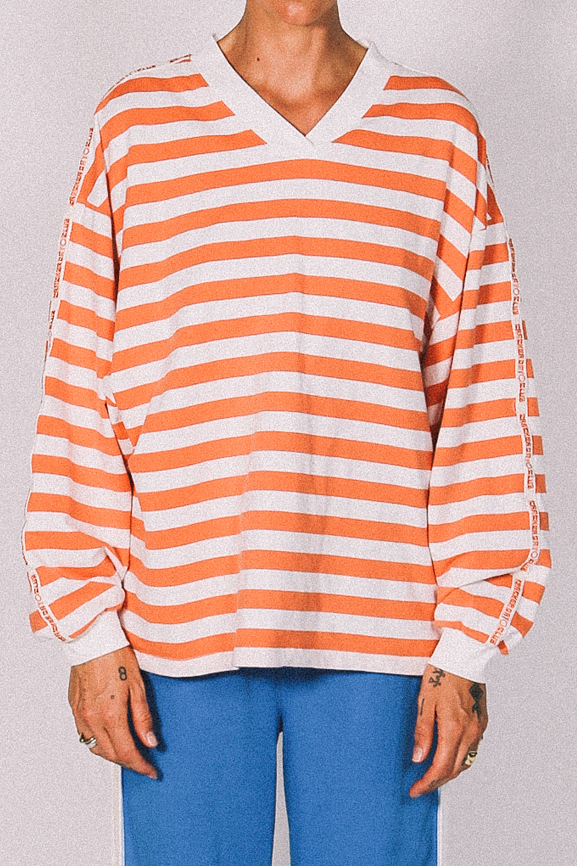 Person wearing an orange and white striped long-sleeve shirt with blue pants on a plain background