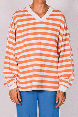 Person wearing an orange and white striped long-sleeve shirt with blue pants on a plain background