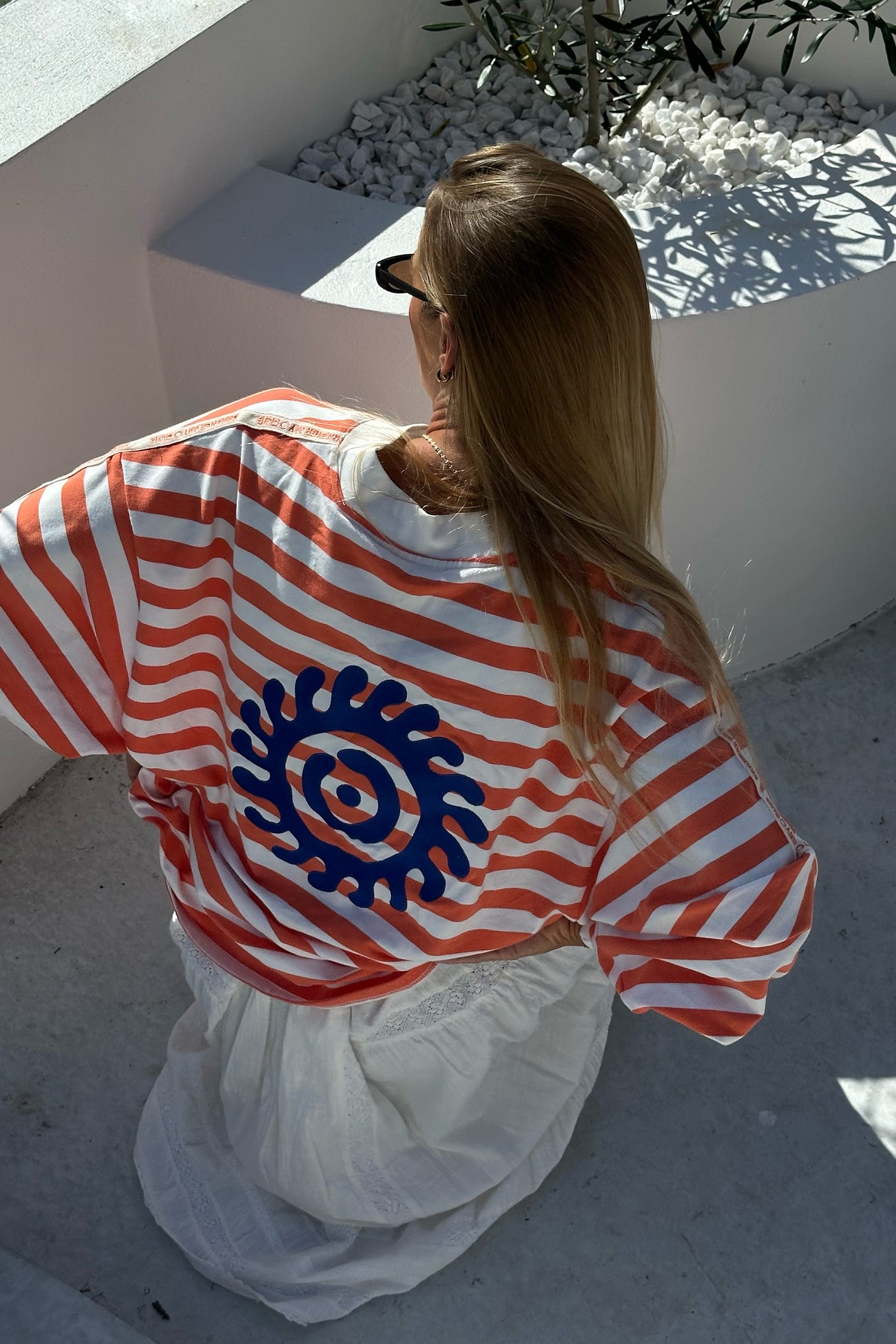 Person wearing a orange and white striped shirt with a blue circular design, standing on a white surface.