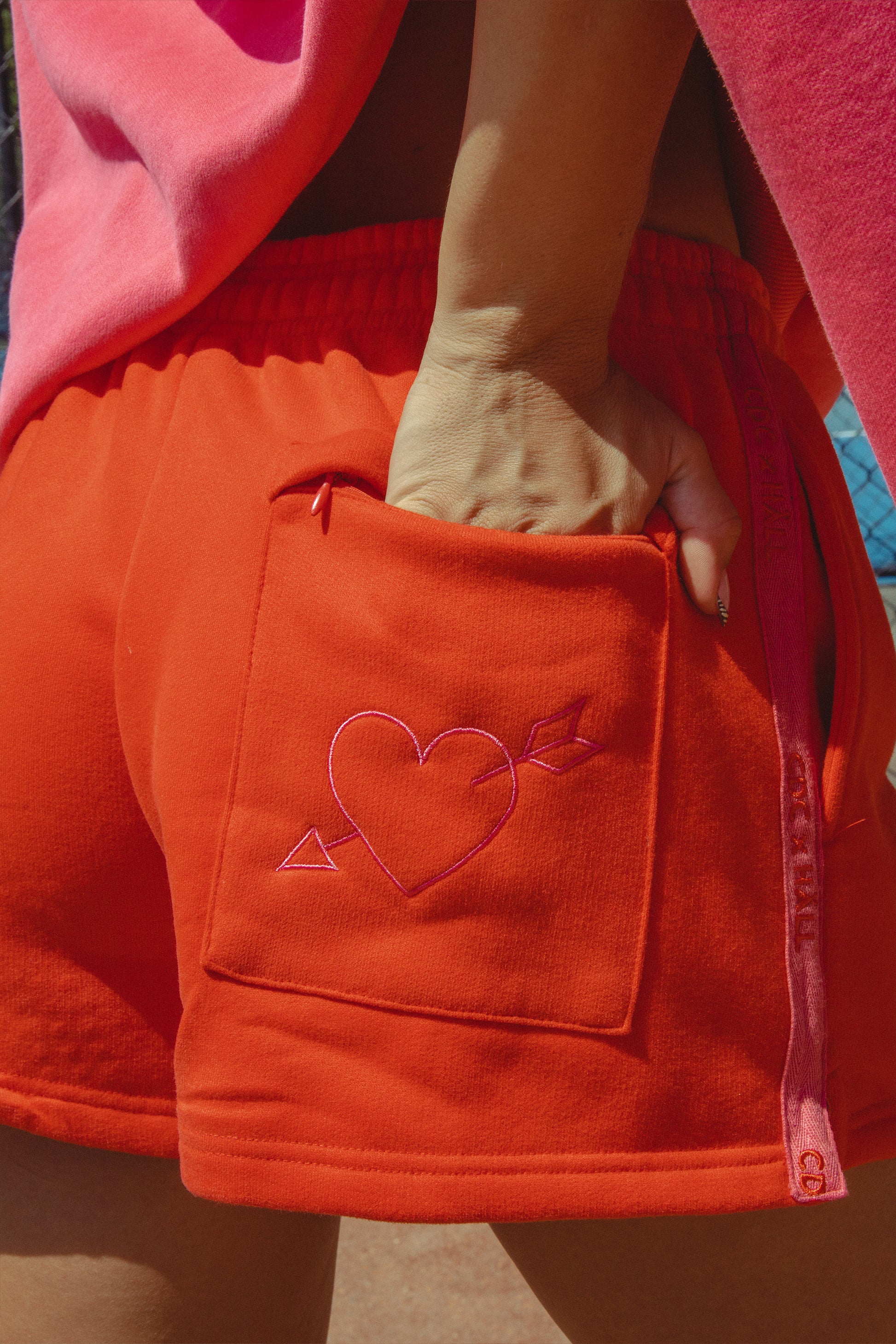 Red shorts with a heart design on the pocket held by a person wearing a pink sweater.