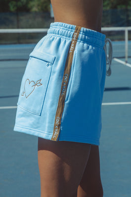 Blue shorts with embroidery and a cracker day club and hall store logo on a tennis court