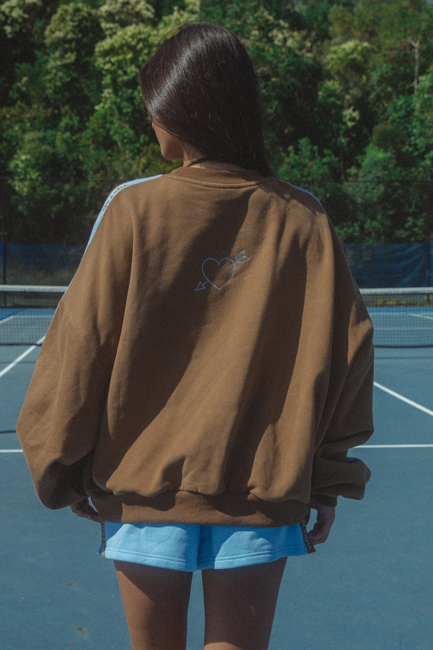 Person wearing a brown pullover sweater with a heart design on a tennis court