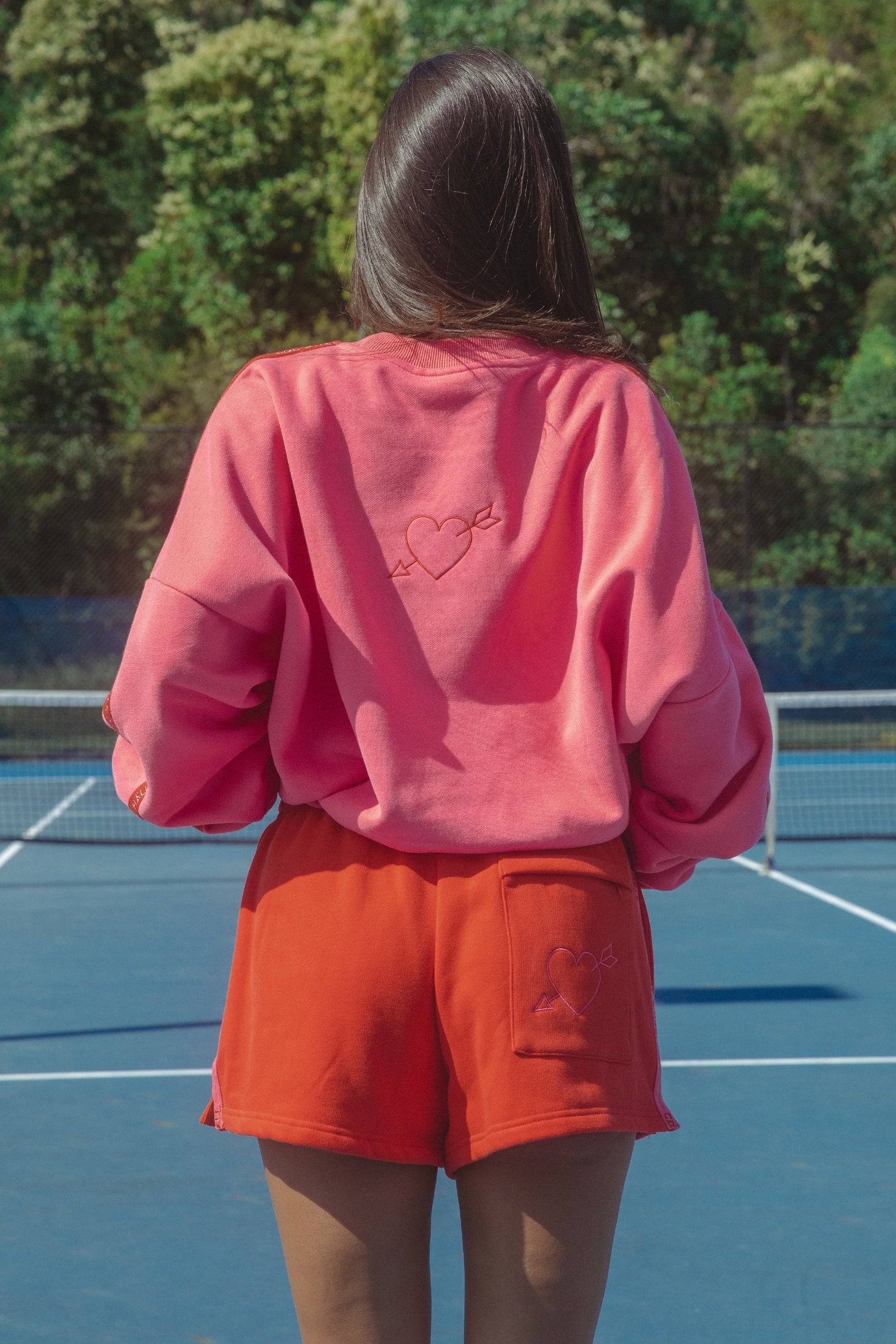 Person wearing a pink sweatshirt and watermelon shorts on a tennis court