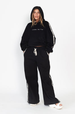 Person wearing a black tracksuit with white stripes on a white background