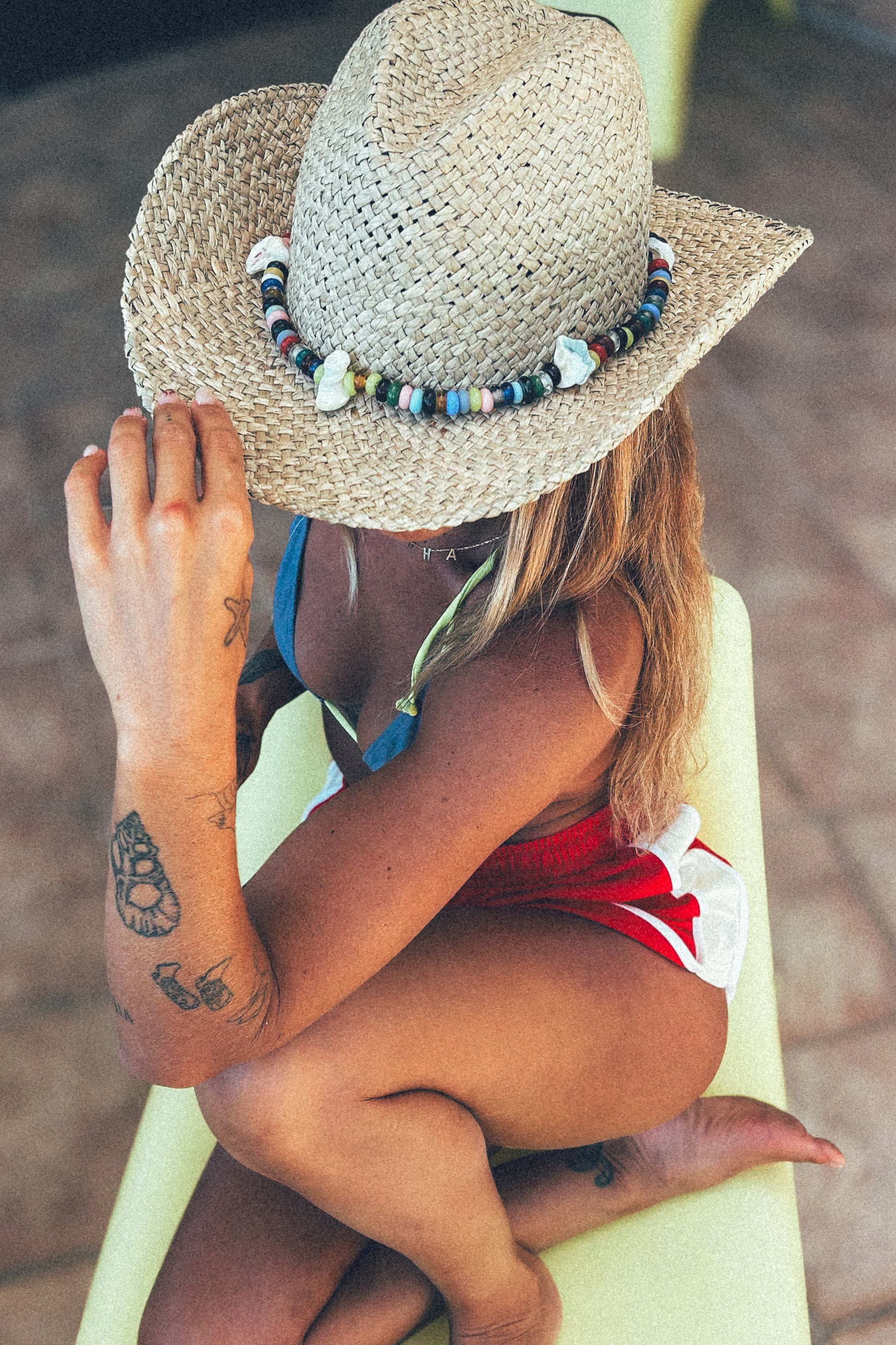 Woman wearing a straw hat with beads and a red swimsuit, sitting on a yellow chair.