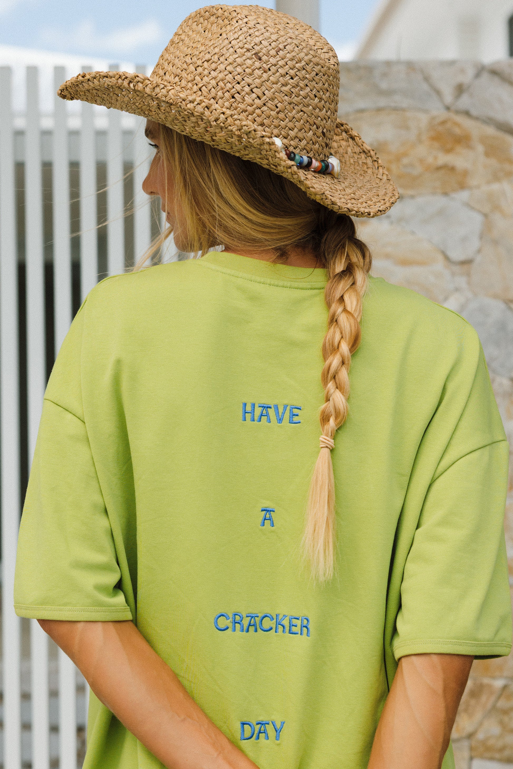 Person wearing a straw hat and green t-shirt with text, standing outdoors.