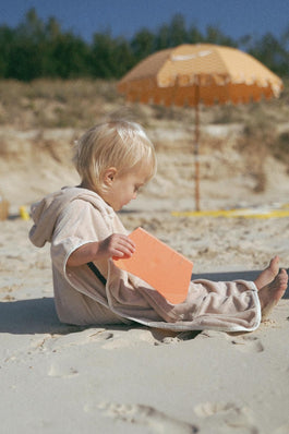 toddler wearing a retro hoodie towel by cracker day club while sitting in the sand on the beach playing with beach toys