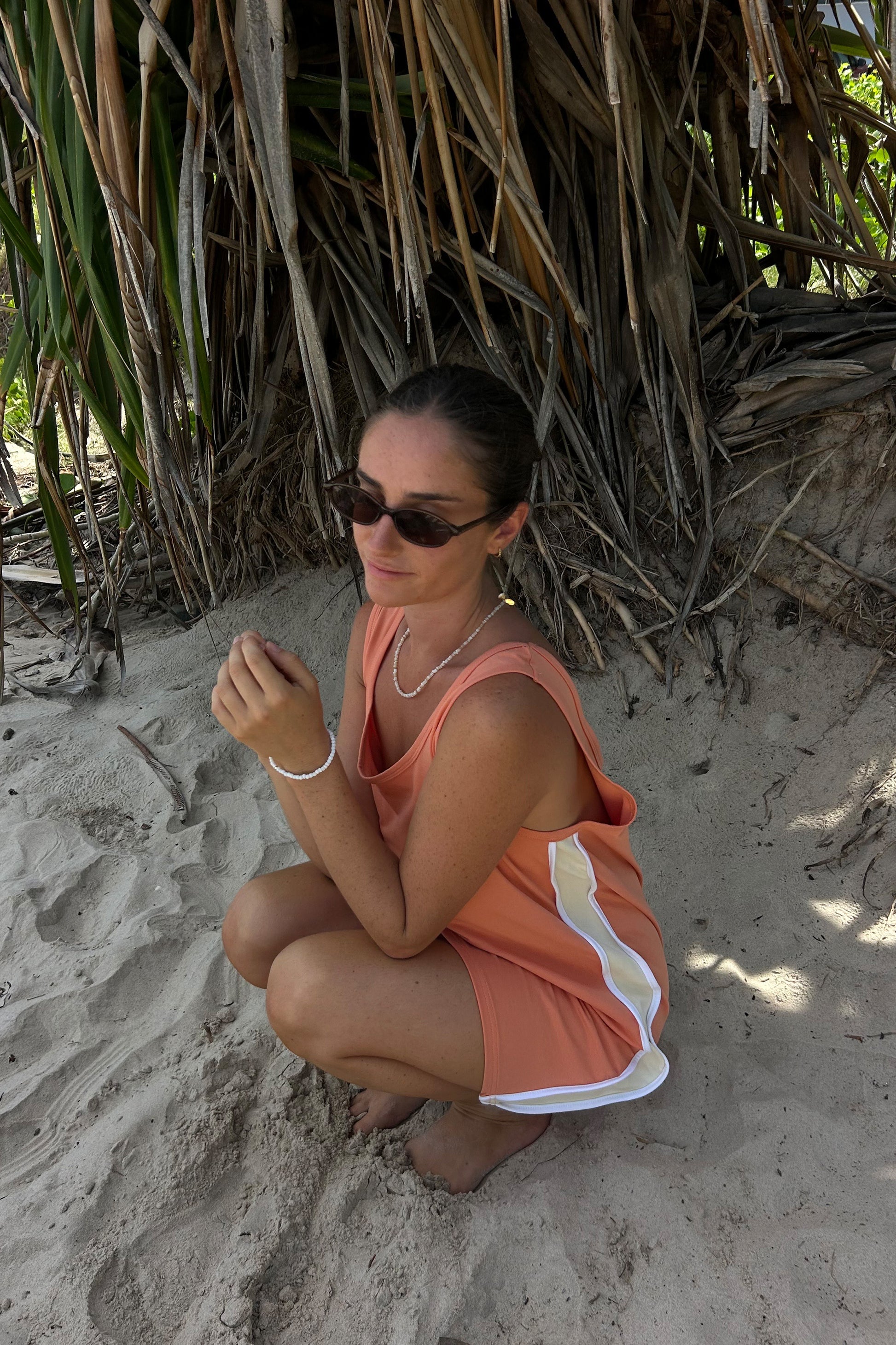 sitting on the beach in a peach coloured dress by cracker day club