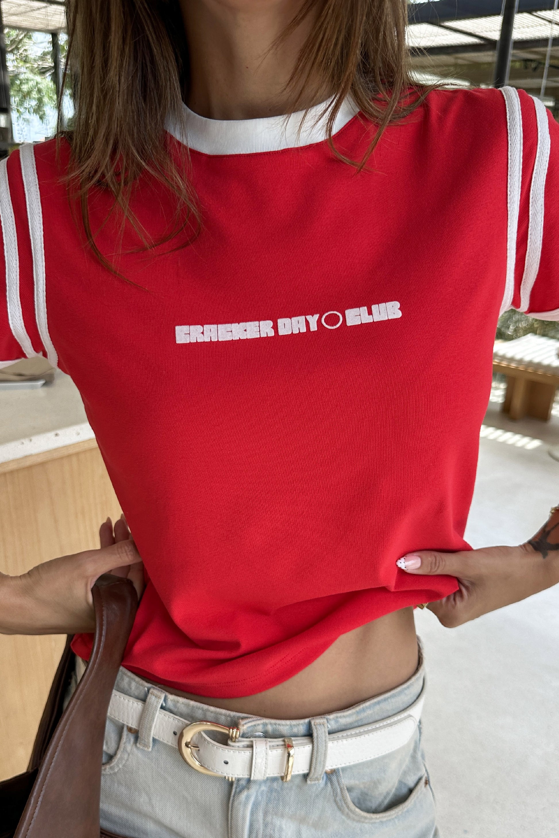 woman wearing a red racer baby tee by cracker day club with jeans 