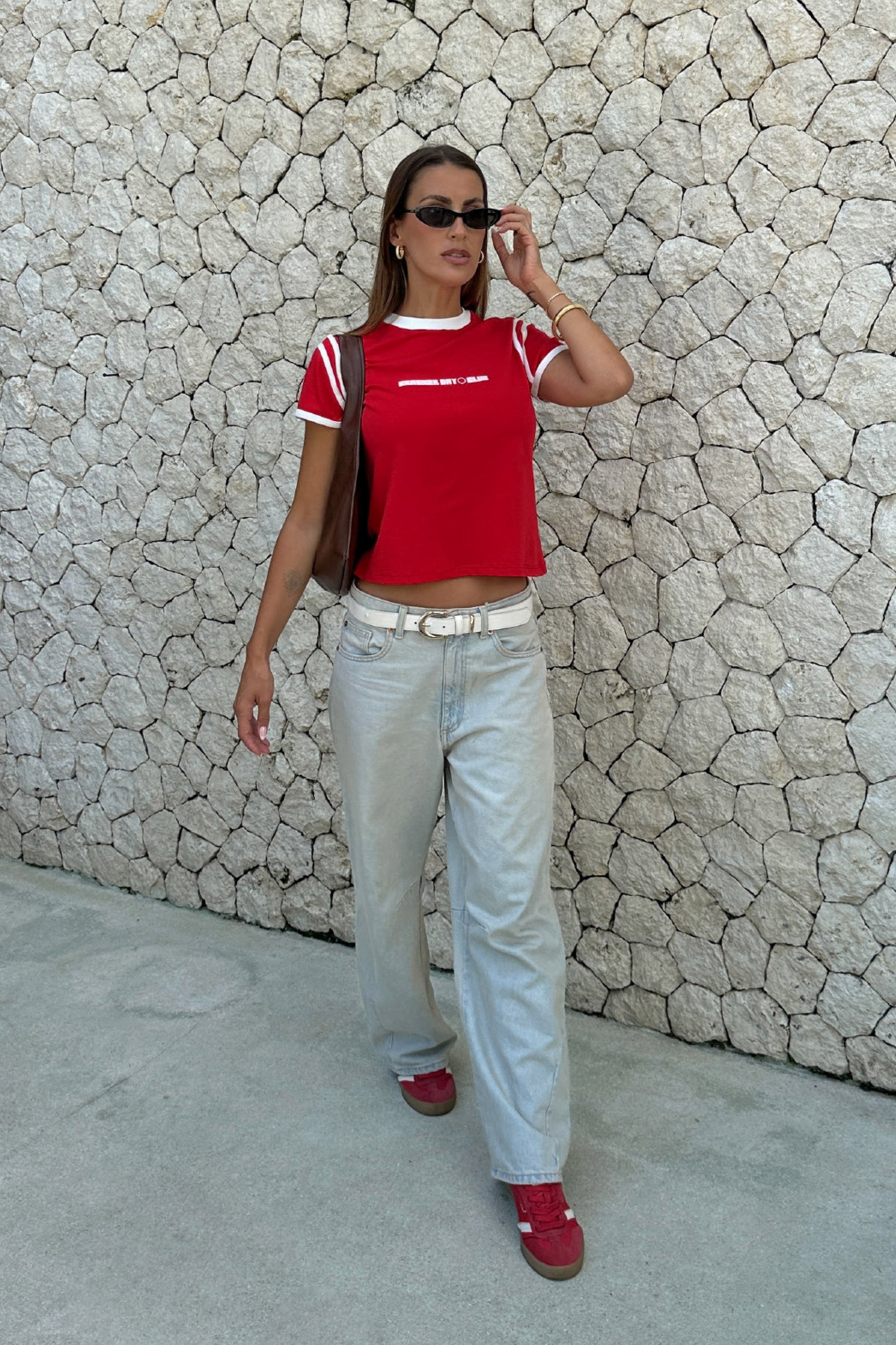 woman wearing a red racer baby tee by cracker day club with jeans  walking down the street