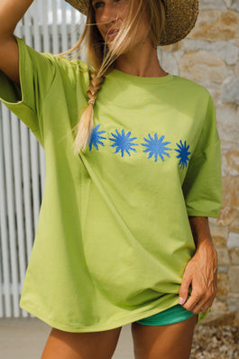 Woman wearing a green t-shirt with blue star designs against a stone wall.