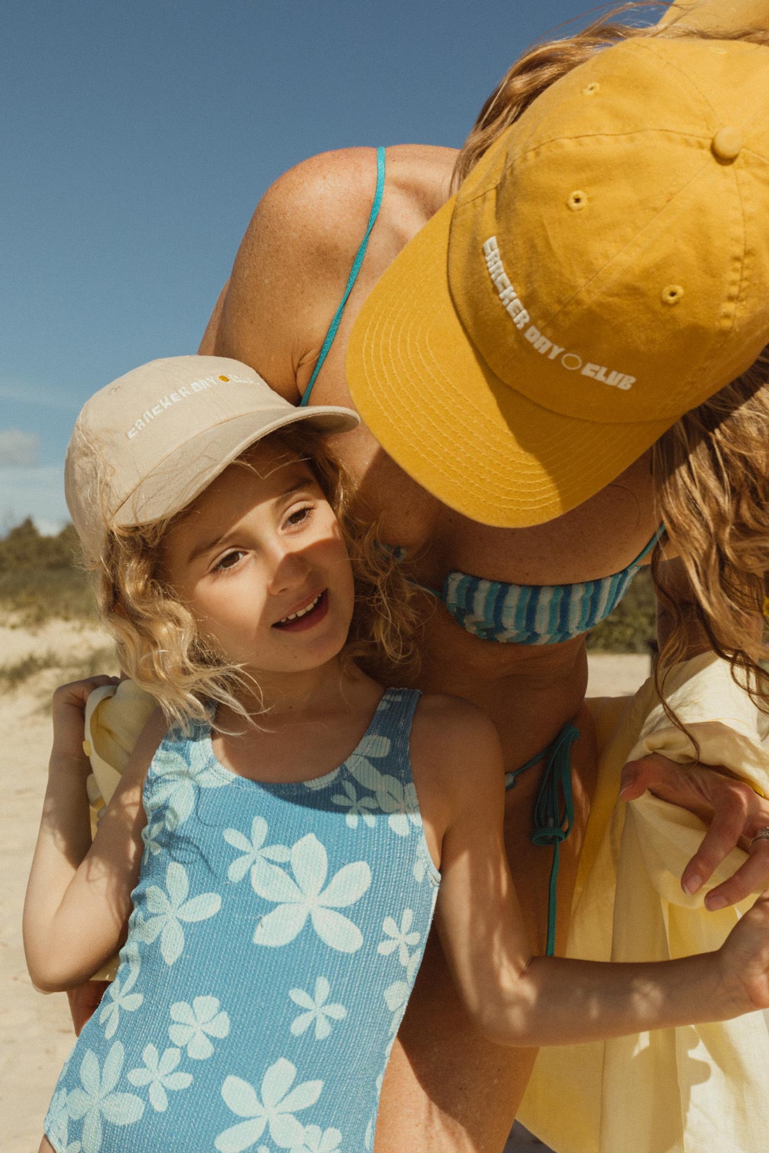 mum in mustard cap at the beach with her daughter playing in the sand