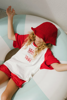 Child wearing a red outfit with a white shirt featuring text, lying on a light-colored surface.